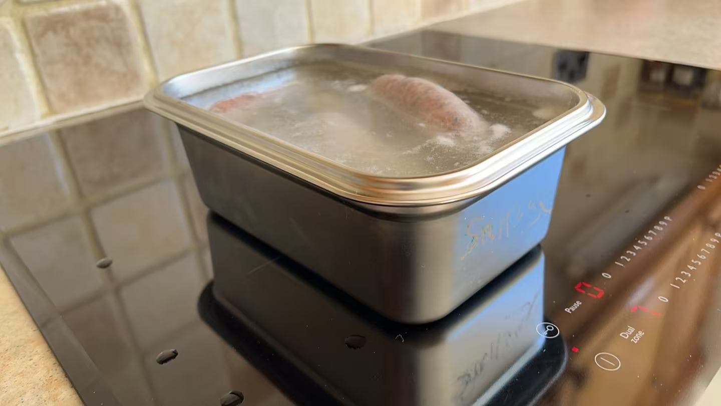 Golden browned sausages in a Loopware stainless steel cooking container